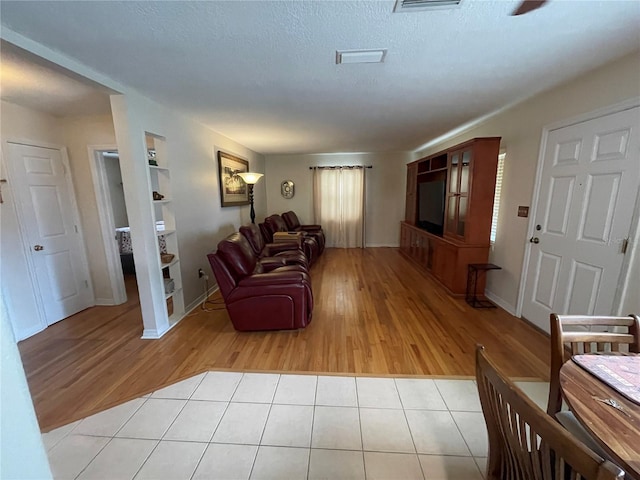 living room featuring a textured ceiling, built in features, and light hardwood / wood-style floors