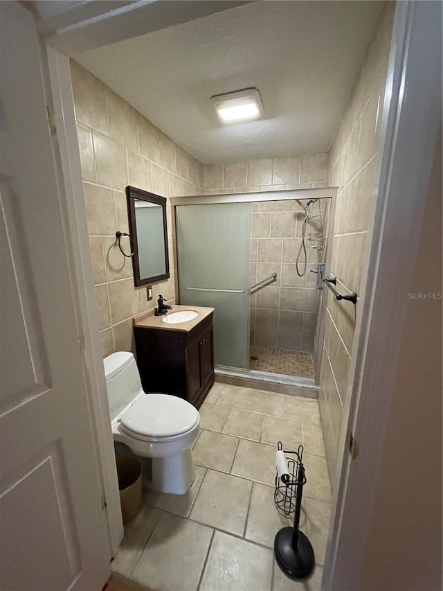 bathroom featuring tile patterned flooring, walk in shower, toilet, tile walls, and vanity