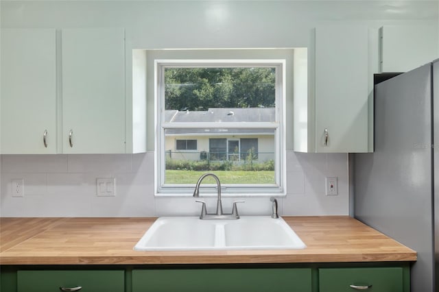 kitchen with stainless steel fridge, green cabinets, sink, butcher block counters, and decorative backsplash