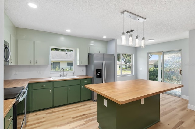 kitchen with light wood-type flooring, a kitchen island, green cabinets, sink, and stainless steel appliances