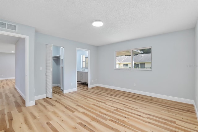 unfurnished bedroom with a spacious closet, a closet, connected bathroom, light hardwood / wood-style flooring, and a textured ceiling