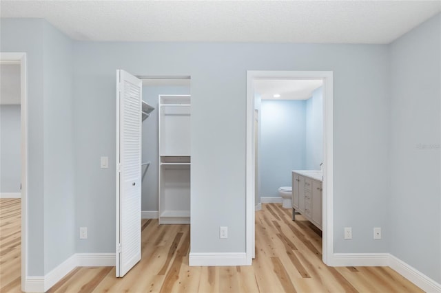 unfurnished bedroom with a spacious closet, a closet, light wood-type flooring, and ensuite bath