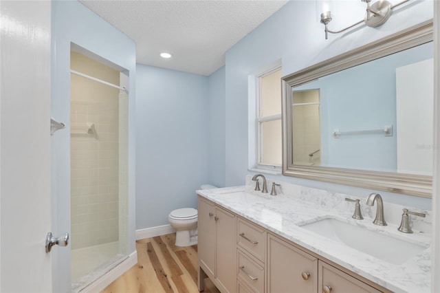 bathroom featuring vanity, wood-type flooring, tiled shower, toilet, and a textured ceiling