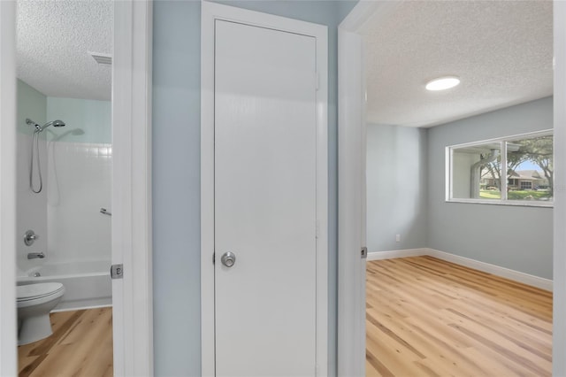 bathroom featuring hardwood / wood-style floors, shower / bathtub combination, toilet, and a textured ceiling