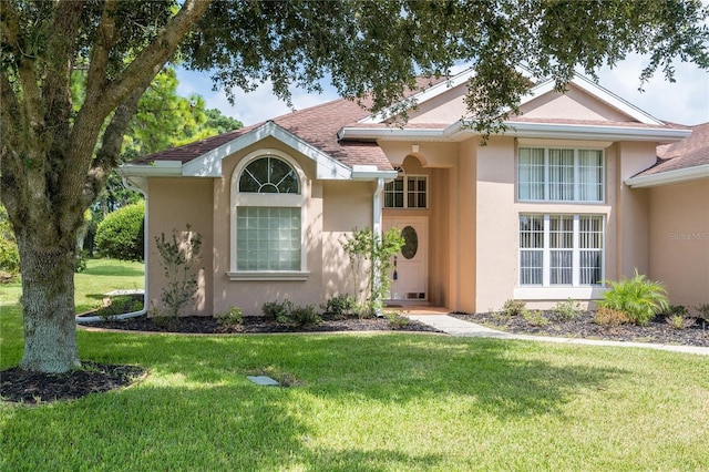 view of front of house with stucco siding, a shingled roof, and a front lawn