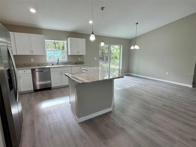 kitchen featuring decorative light fixtures, hardwood / wood-style floors, light stone countertops, stainless steel appliances, and white cabinets