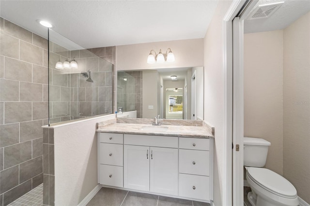 bathroom featuring toilet, tile patterned flooring, tiled shower, and vanity