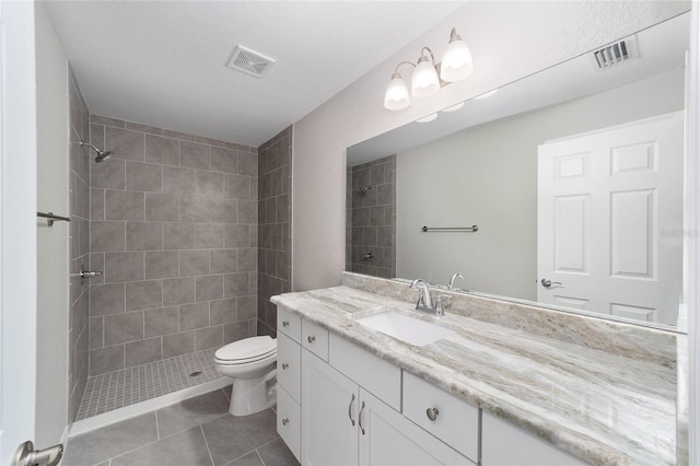 bathroom with toilet, vanity, tiled shower, and tile patterned flooring