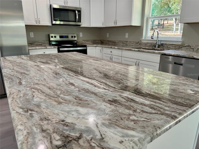 kitchen with light stone countertops, appliances with stainless steel finishes, a kitchen island, white cabinetry, and sink