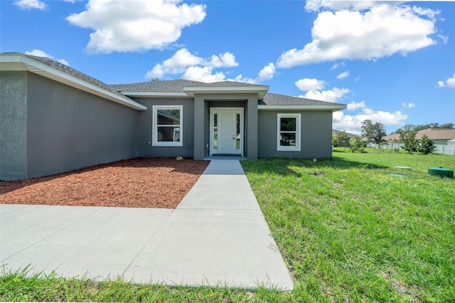 view of front of property with roof with shingles, a front lawn, and stucco siding