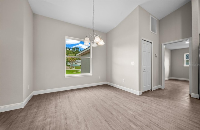 empty room with an inviting chandelier, hardwood / wood-style floors, and high vaulted ceiling