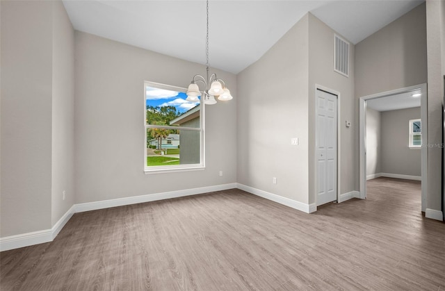 unfurnished room with a healthy amount of sunlight, a chandelier, wood finished floors, and visible vents