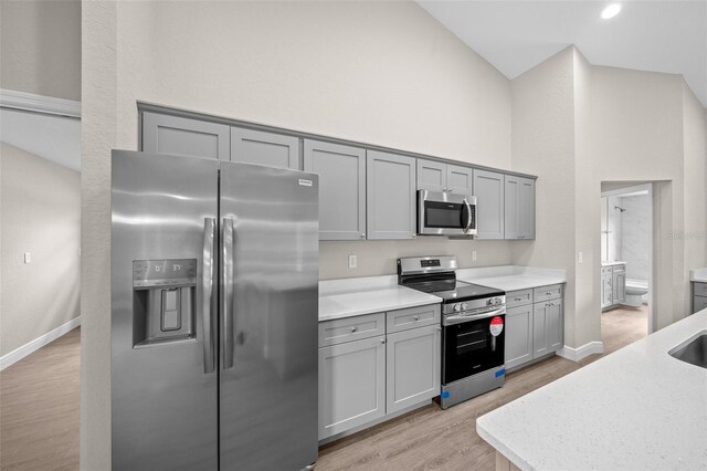 kitchen featuring light hardwood / wood-style floors, gray cabinetry, appliances with stainless steel finishes, light stone counters, and high vaulted ceiling