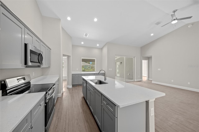 kitchen with lofted ceiling, a center island with sink, sink, gray cabinets, and stainless steel appliances