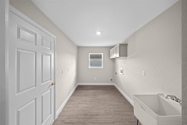 laundry area featuring a textured wall, cabinet space, a sink, and washer hookup