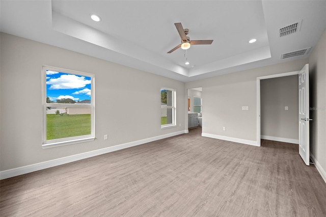 unfurnished bedroom featuring a tray ceiling, wood finished floors, visible vents, and recessed lighting