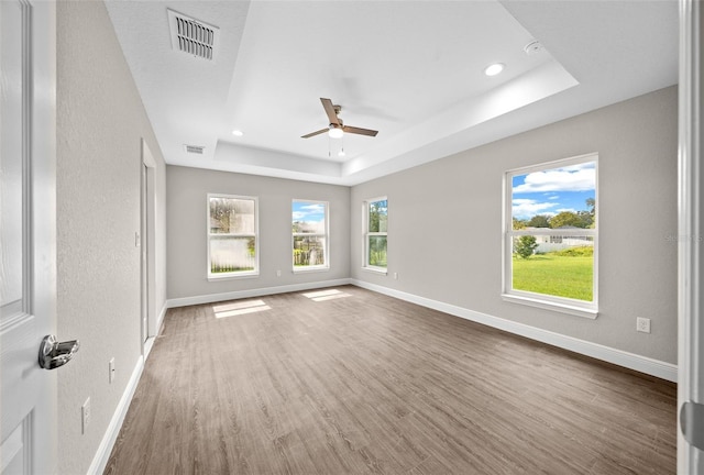 empty room featuring wood finished floors, ceiling fan, a tray ceiling, visible vents, and recessed lighting