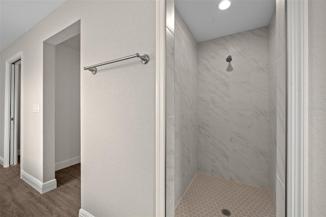 bathroom with recessed lighting, baseboards, wood finished floors, and tiled shower
