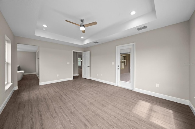 unfurnished bedroom with ensuite bathroom, hardwood / wood-style flooring, a tray ceiling, and ceiling fan