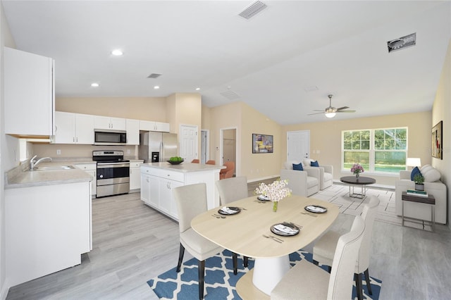 dining room featuring ceiling fan, sink, light wood-type flooring, and vaulted ceiling