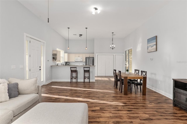 living room featuring dark wood-type flooring, a high ceiling, sink, and an inviting chandelier