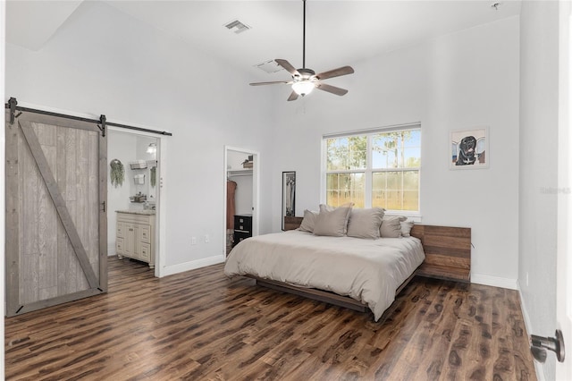 bedroom with ceiling fan, dark wood-type flooring, a barn door, a spacious closet, and connected bathroom