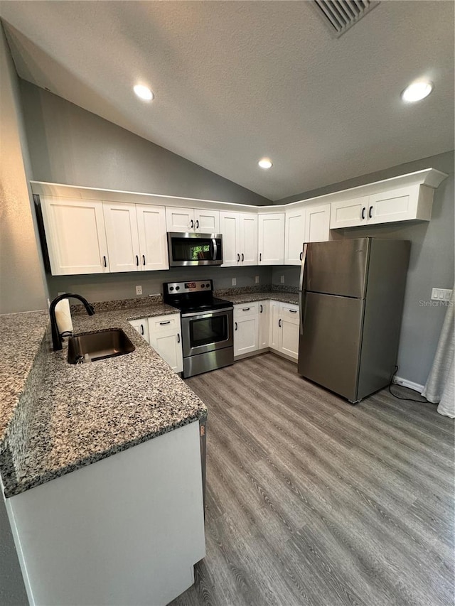 kitchen with lofted ceiling, white cabinets, appliances with stainless steel finishes, light wood-type flooring, and sink