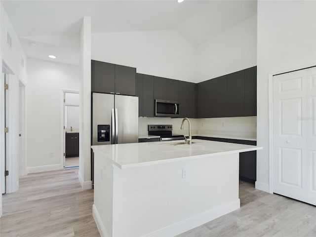 kitchen with high vaulted ceiling, sink, stainless steel appliances, a center island with sink, and light wood-type flooring