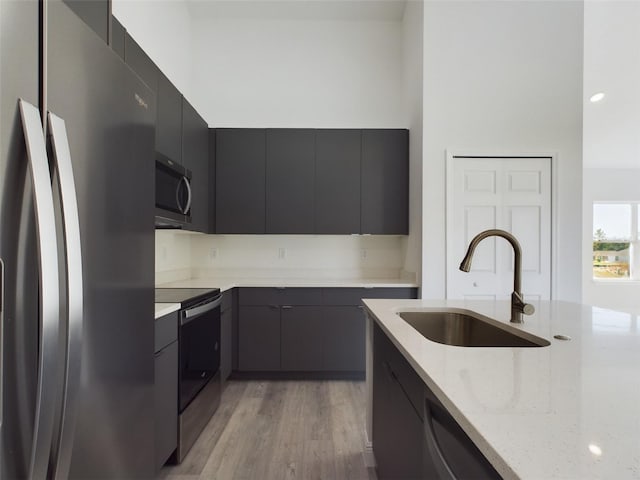 kitchen featuring stainless steel appliances, sink, light stone counters, and light hardwood / wood-style flooring