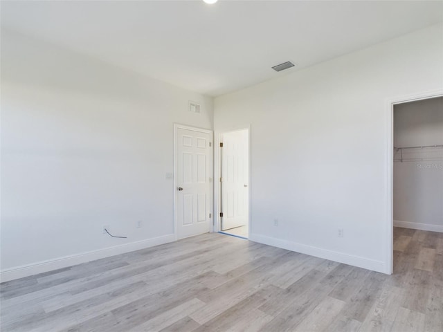 unfurnished bedroom featuring a walk in closet, a closet, and light hardwood / wood-style flooring