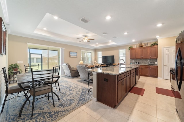 kitchen featuring dishwasher, an island with sink, backsplash, light tile patterned flooring, and light stone counters