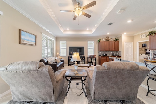 tiled living room with ceiling fan, a raised ceiling, and ornamental molding