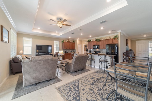 tiled living room with ornamental molding, ceiling fan, and a raised ceiling