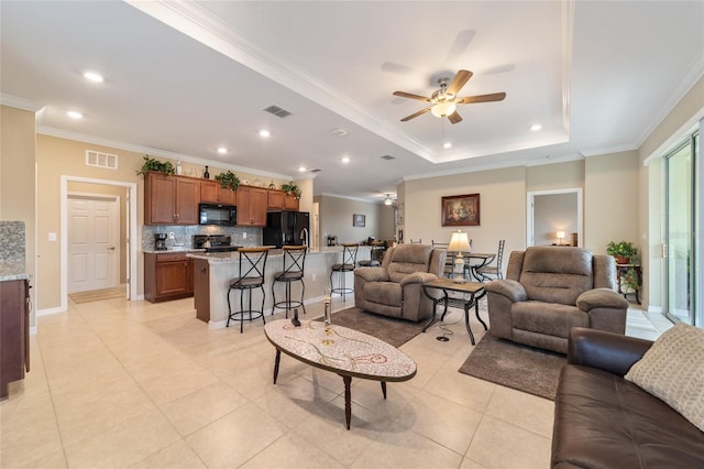 tiled living room with ceiling fan, ornamental molding, and a tray ceiling