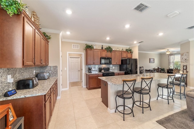 kitchen with black appliances, a kitchen island with sink, crown molding, and a breakfast bar