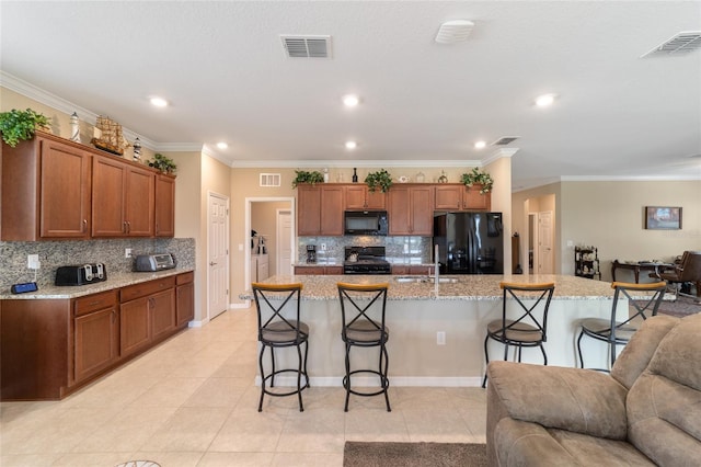 kitchen featuring decorative backsplash, a center island with sink, ornamental molding, black appliances, and a breakfast bar