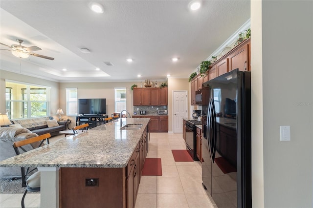 kitchen with a large island with sink, light tile patterned floors, black appliances, sink, and a breakfast bar area