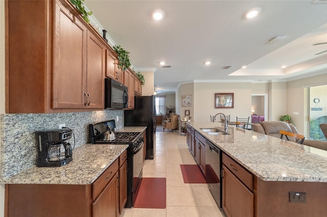 kitchen with a large island, light stone countertops, black appliances, crown molding, and sink