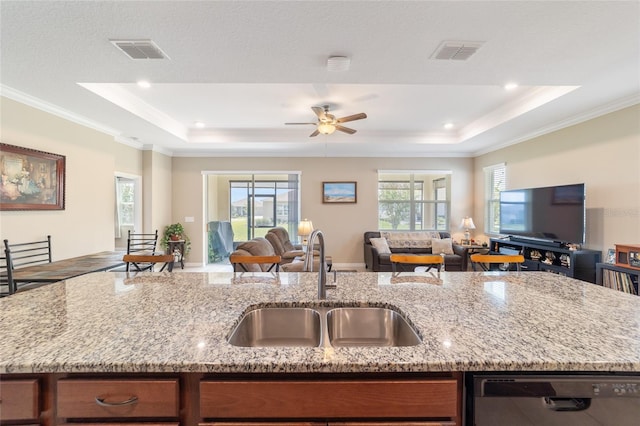 kitchen with dishwasher, an island with sink, sink, light stone countertops, and a raised ceiling