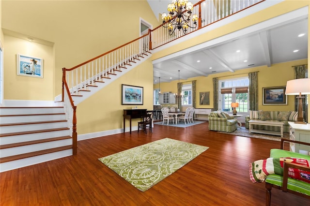 living room with a towering ceiling, beamed ceiling, a notable chandelier, and hardwood / wood-style flooring