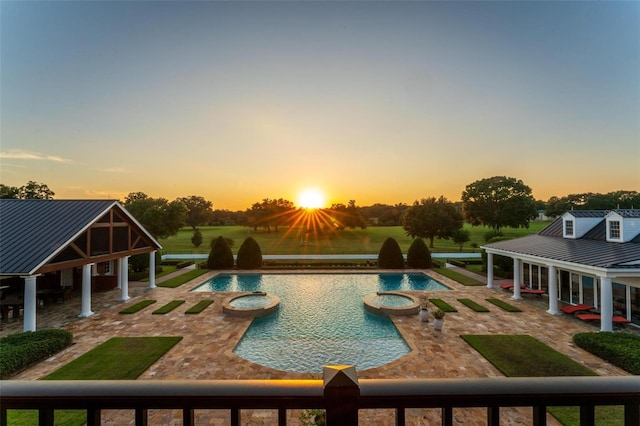 pool at dusk featuring a pool with connected hot tub, a patio area, and a lawn