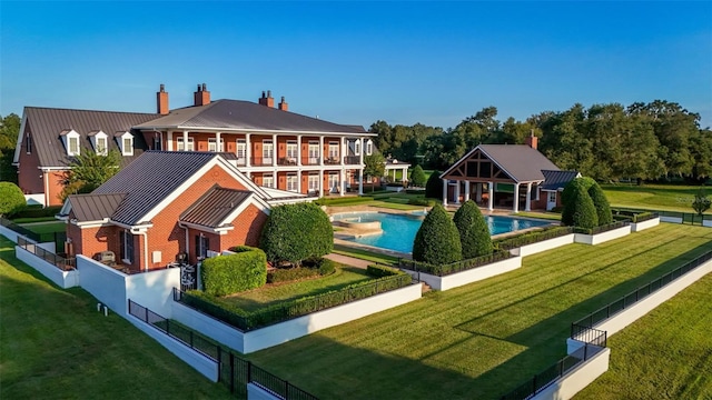 rear view of property featuring an outdoor pool, a standing seam roof, brick siding, and a yard