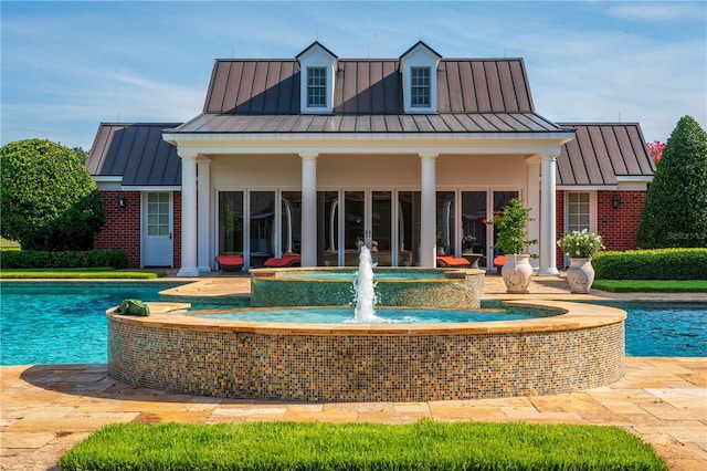 back of property featuring a pool with connected hot tub, a standing seam roof, brick siding, and metal roof