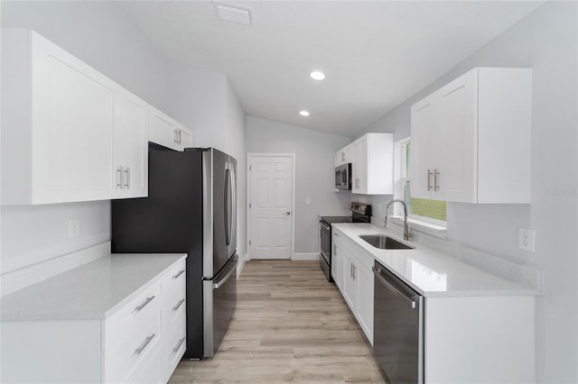 kitchen featuring stainless steel appliances, lofted ceiling, white cabinets, and a sink