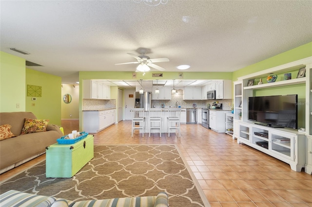 living room with a textured ceiling, sink, light tile patterned floors, and ceiling fan