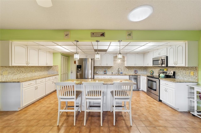 kitchen featuring white cabinets, hanging light fixtures, light stone counters, stainless steel appliances, and sink