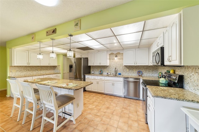 kitchen featuring light stone counters, white cabinetry, stainless steel appliances, pendant lighting, and a center island