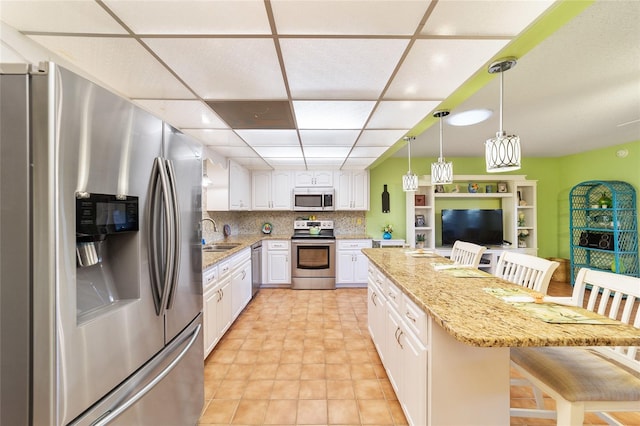 kitchen featuring white cabinets, a breakfast bar area, light stone countertops, pendant lighting, and stainless steel appliances