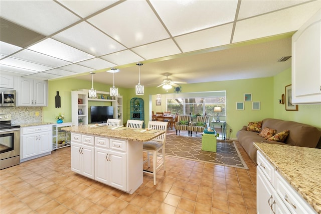 kitchen with a breakfast bar area, stainless steel appliances, a center island, decorative light fixtures, and white cabinetry