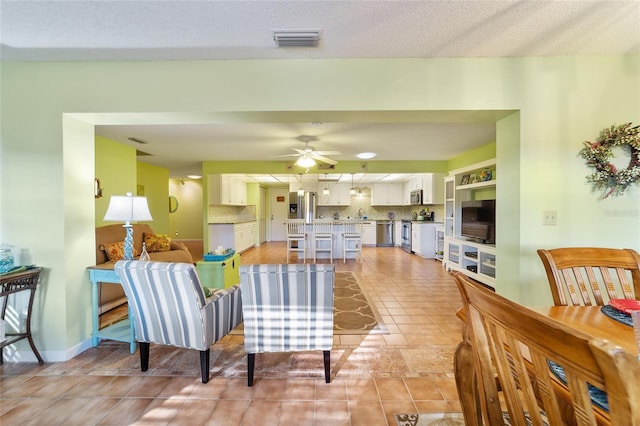 living room featuring a textured ceiling, light tile patterned floors, and ceiling fan